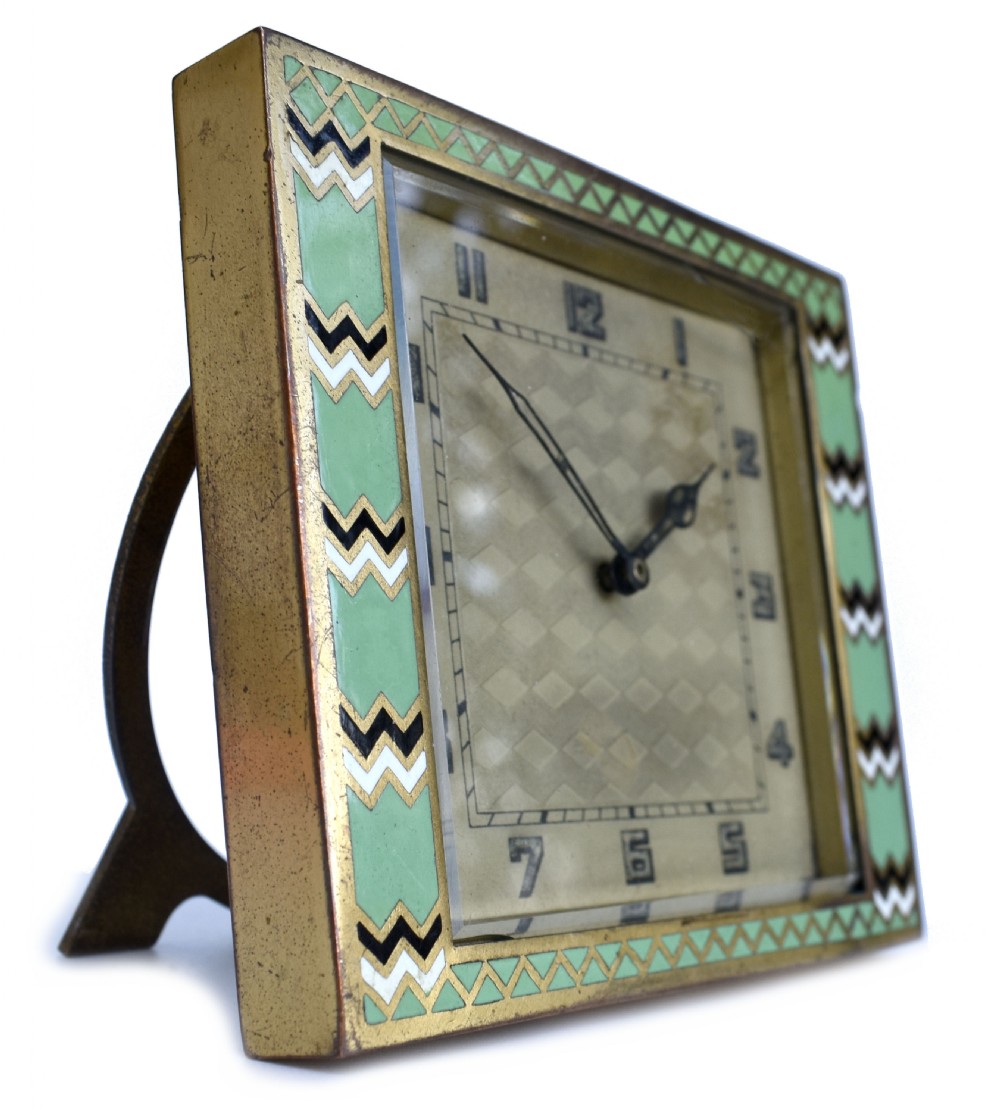 A square Art Deco clock featuring a green, white, and black chevron enamel border surrounding a geometric patterned metal dial with Arabic numerals. View V