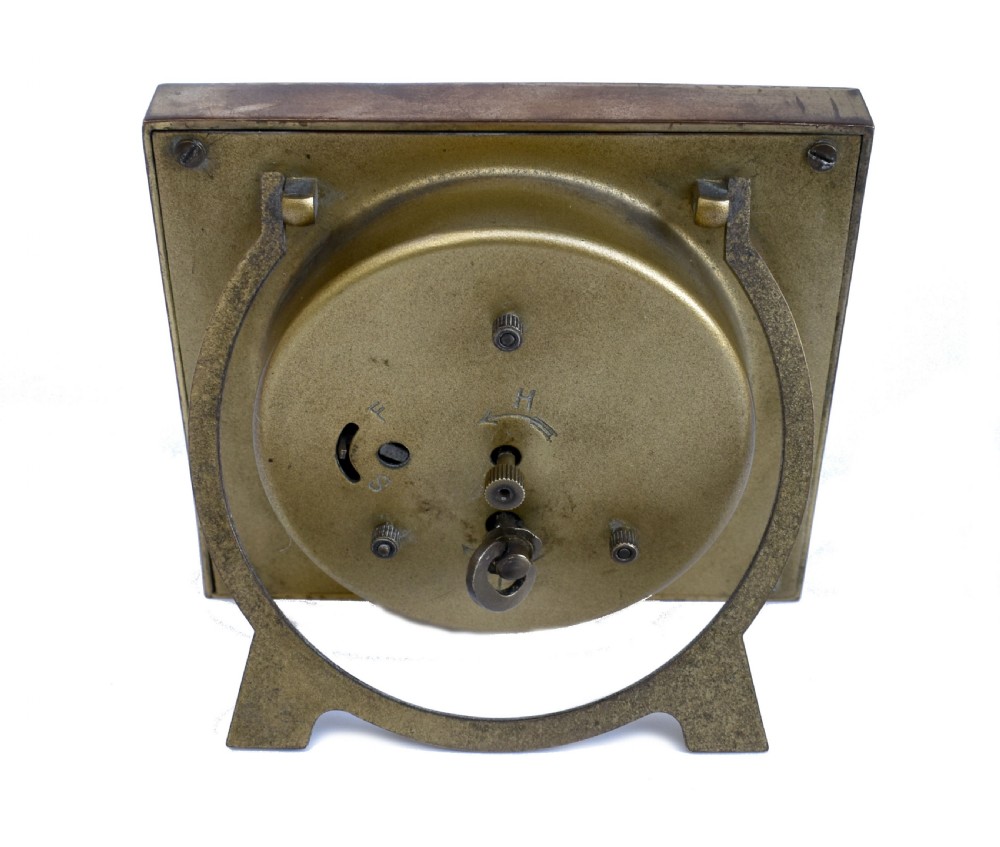 A square Art Deco clock featuring a green, white, and black chevron enamel border surrounding a geometric patterned metal dial with Arabic numerals. View VII