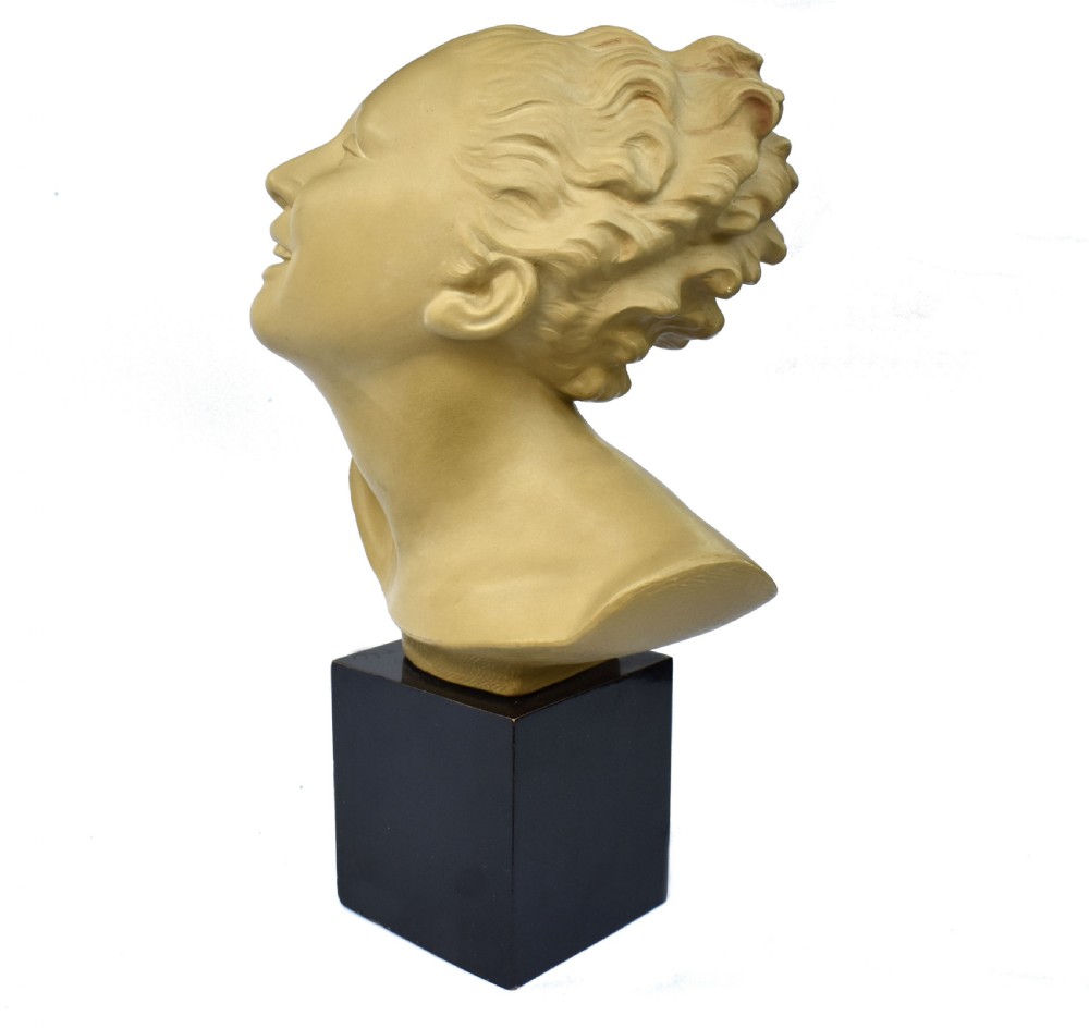 A terracotta Art Deco female bust depicting a woman with swept-back wavy hair looking upwards, mounted on a square black wooden plinth.