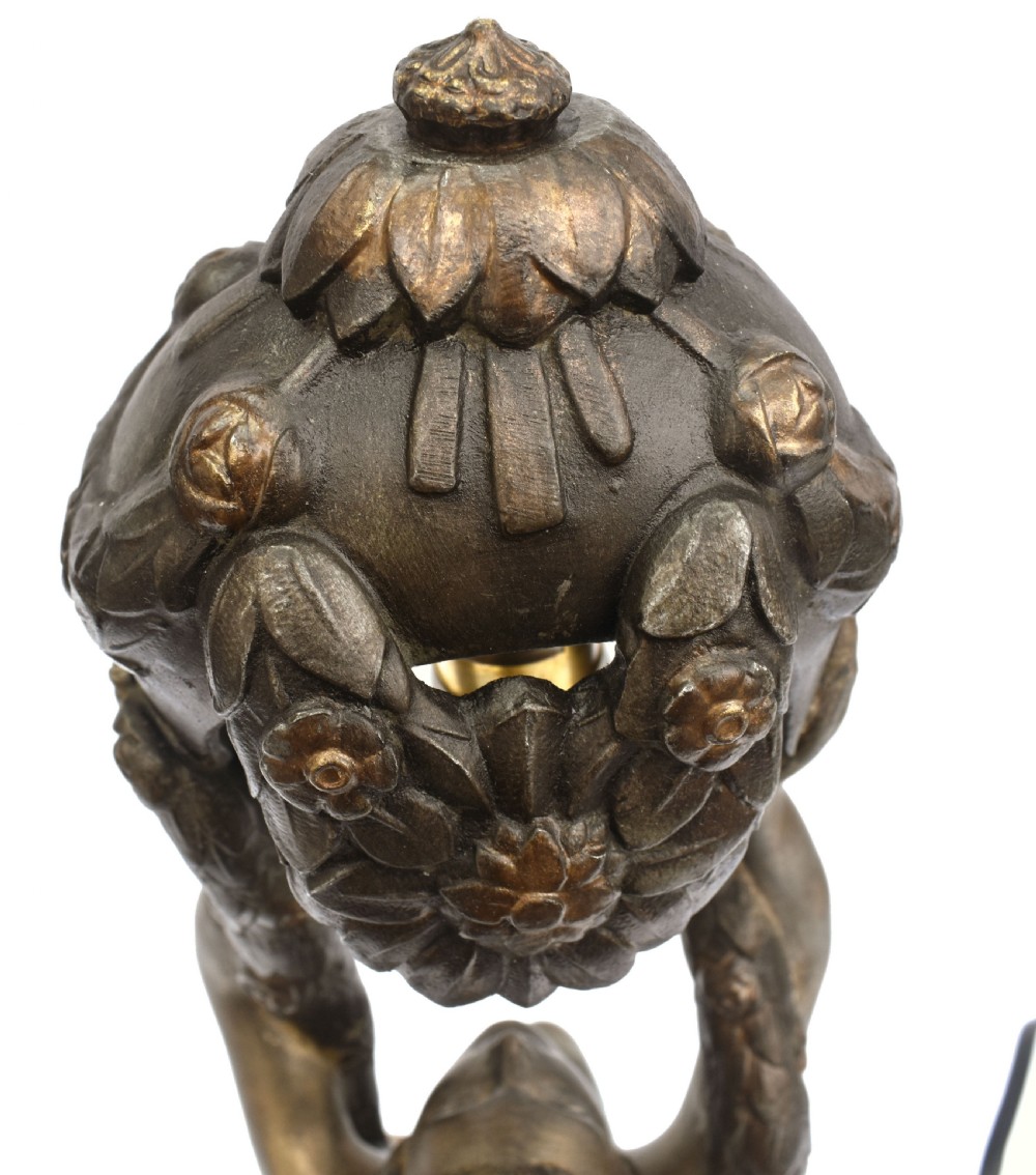 An Art Deco patinated metal table lamp featuring a kneeling female figure holding up a floral garland shade, set on a rectangular marble base. View VIII
