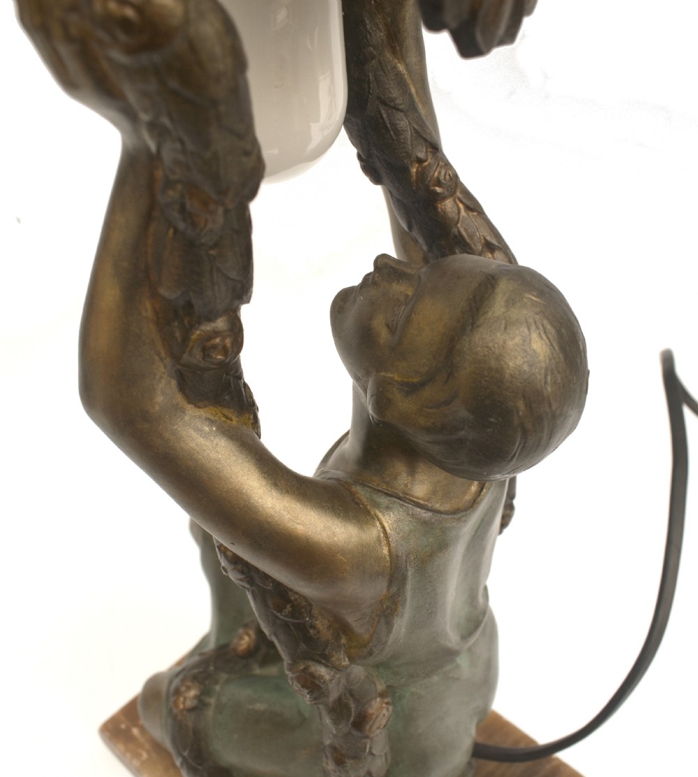An Art Deco patinated metal table lamp featuring a kneeling female figure holding up a floral garland shade, set on a rectangular marble base. View IX