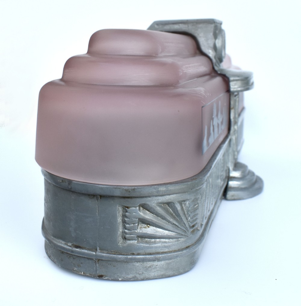 An Art Deco style lamp featuring a stepped pink frosted glass body decorated with black silhouetted figures dining inside windows, framed by a silver-coloured cast metal base and central architectural doorway with a clock motif. View XVII