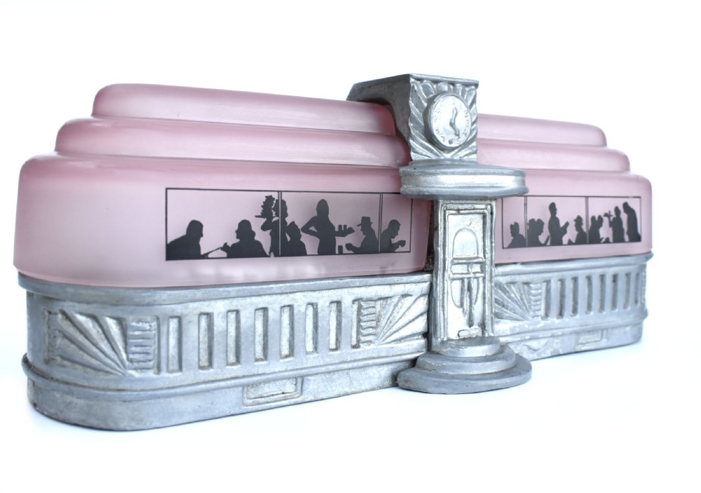 An Art Deco style lamp featuring a stepped pink frosted glass body decorated with black silhouetted figures dining inside windows, framed by a silver-coloured cast metal base and central architectural doorway with a clock motif. View XVIII