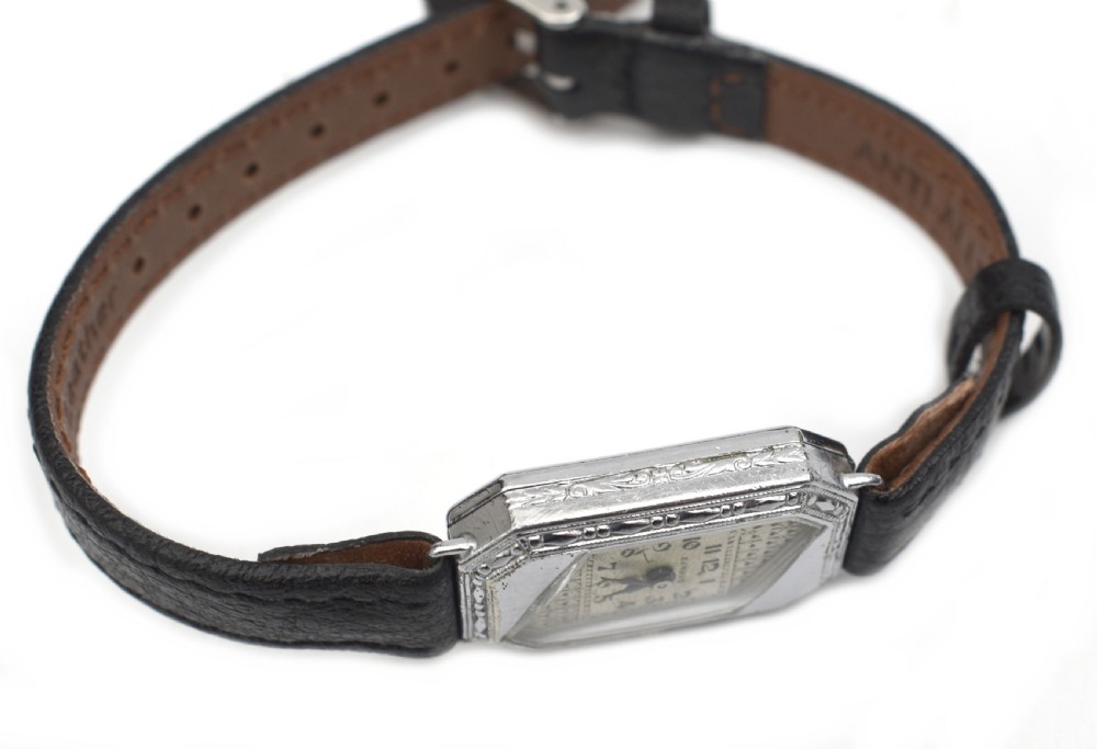 An Art Deco ladies wristwatch featuring an octagonal engraved 14k white gold case, a patterned geometric dial, blue hands, and a black leather strap. View VII