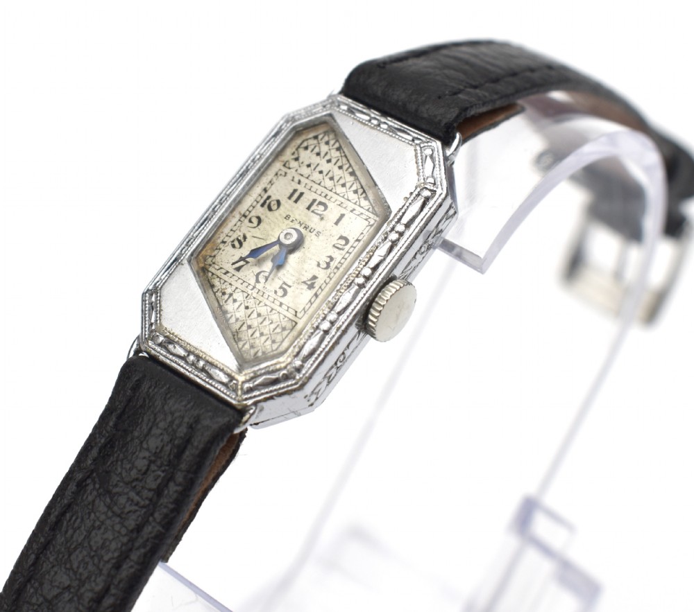 An Art Deco ladies wristwatch featuring an octagonal engraved 14k white gold case, a patterned geometric dial, blue hands, and a black leather strap. View XIV