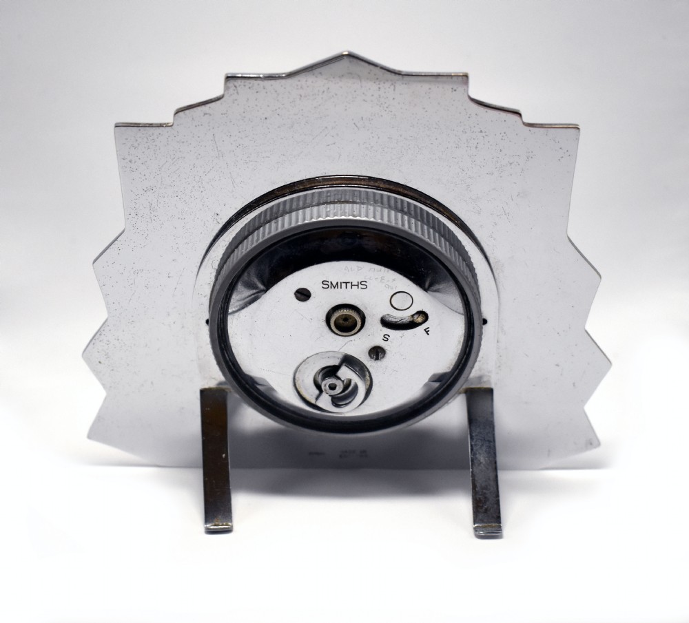 An Art Deco chrome clock featuring a square cream dial, geometric stepped sides, and a sunburst top motif. View VI