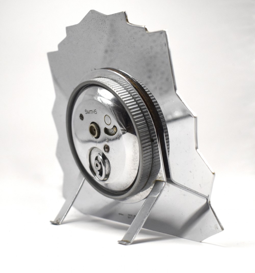 An Art Deco chrome clock featuring a square cream dial, geometric stepped sides, and a sunburst top motif. View IV