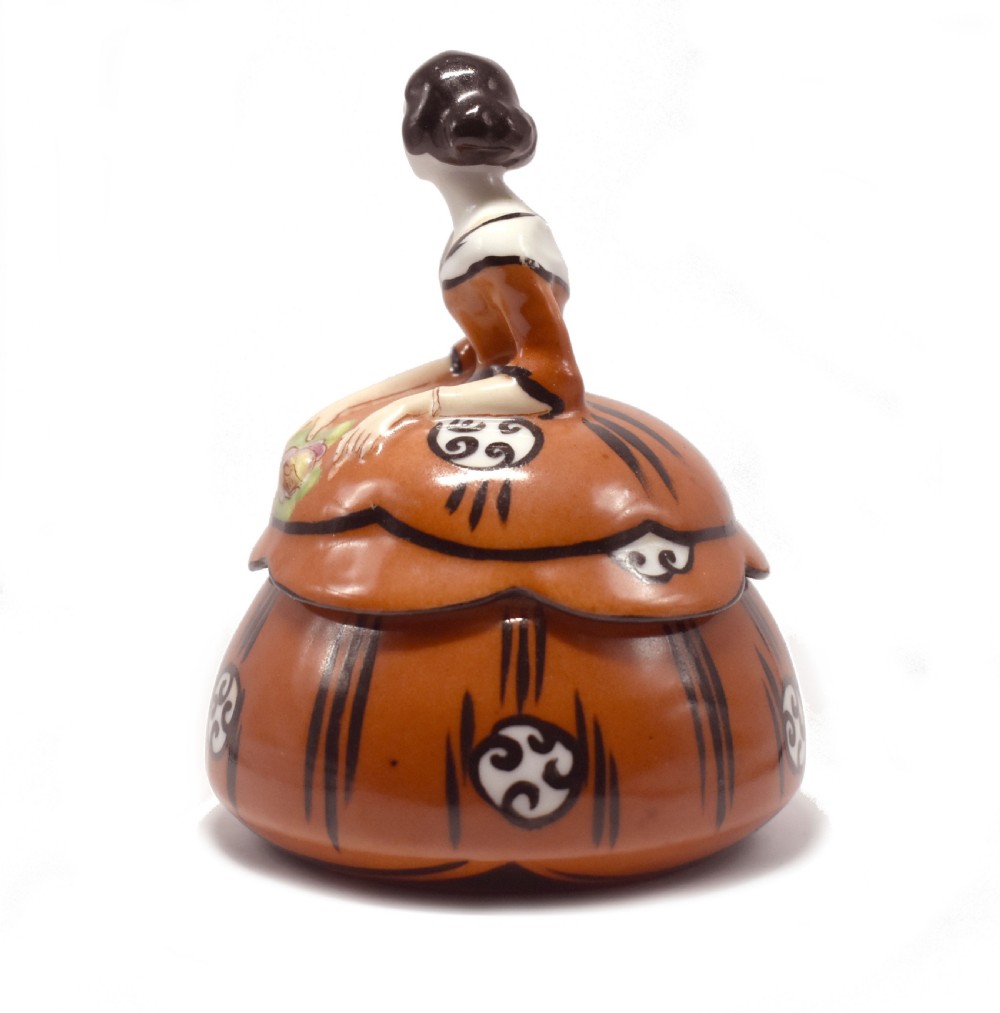 An Art Deco glazed ceramic powder bowl featuring a lid shaped as a lady in a terracotta and black dress holding a flower. View III