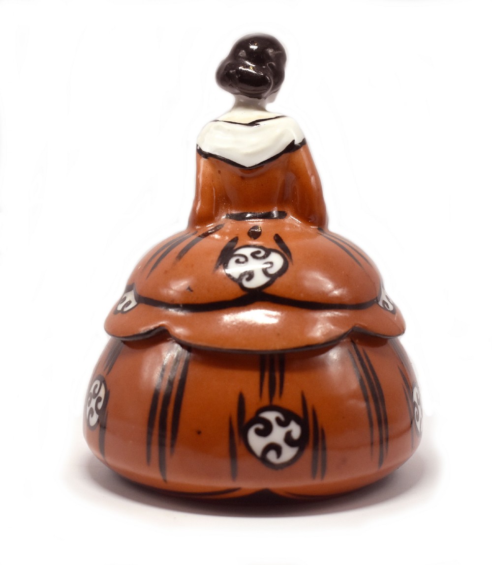 An Art Deco glazed ceramic powder bowl featuring a lid shaped as a lady in a terracotta and black dress holding a flower. View IV