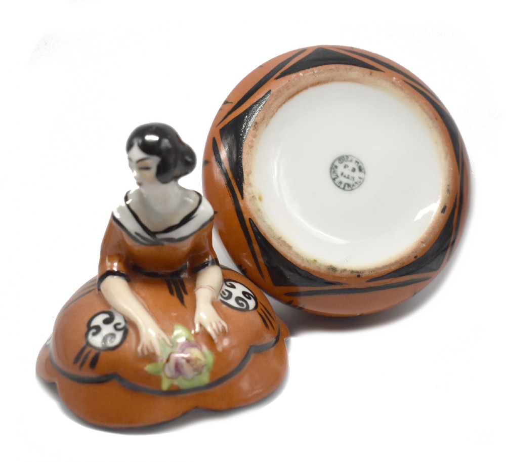 An Art Deco glazed ceramic powder bowl featuring a lid shaped as a lady in a terracotta and black dress holding a flower. View VII