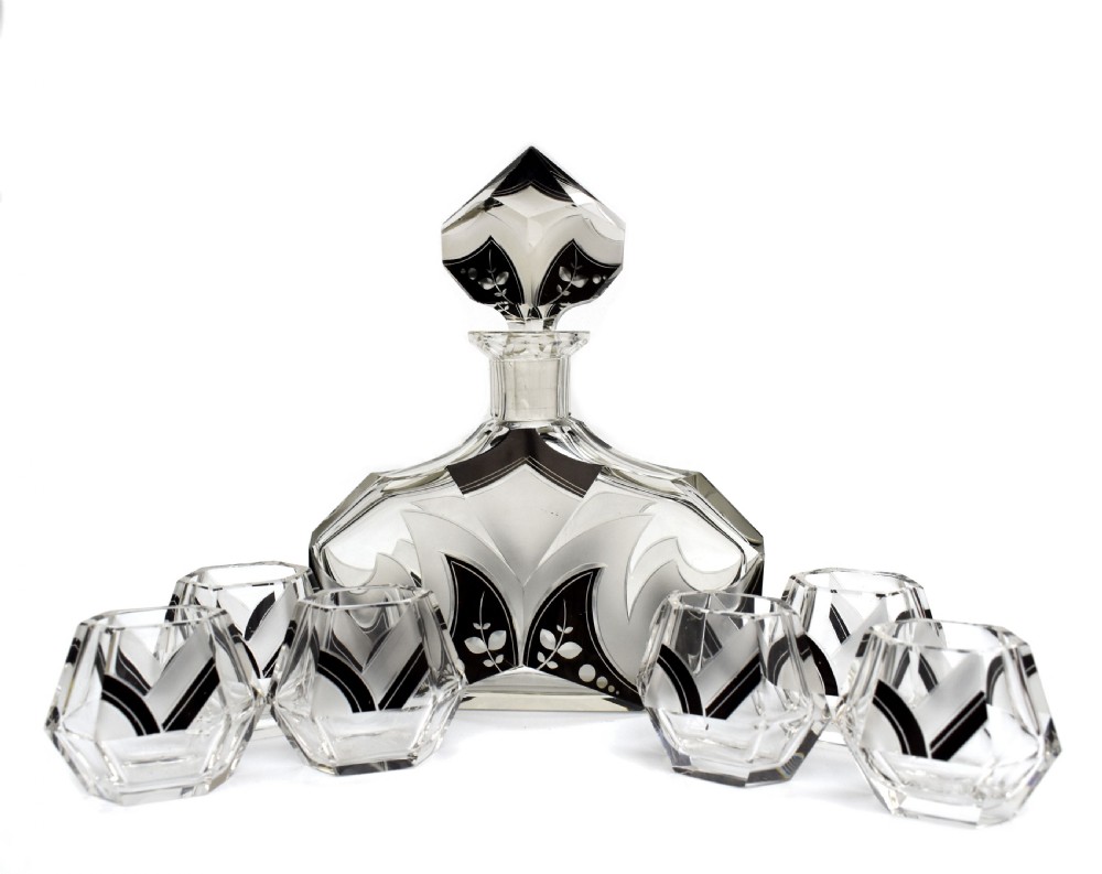 An Art Deco clear glass decanter set featuring black enamelled geometric patterns and frosted accents, accompanied by six matching faceted glasses and a faceted stopper.