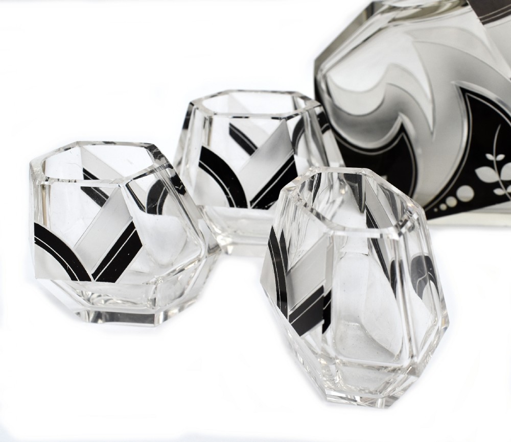 An Art Deco clear glass decanter set featuring black enamelled geometric patterns and frosted accents, accompanied by six matching faceted glasses and a faceted stopper. View VII