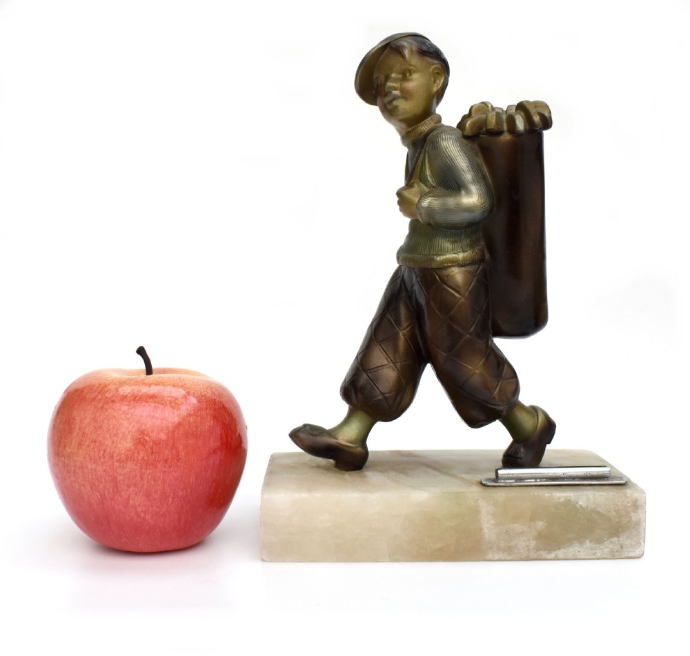 An Art Deco cold-painted bronze sculpture of a golf caddy carrying a bag, mounted on a rectangular cream onyx base with an attached metal lighter striker.