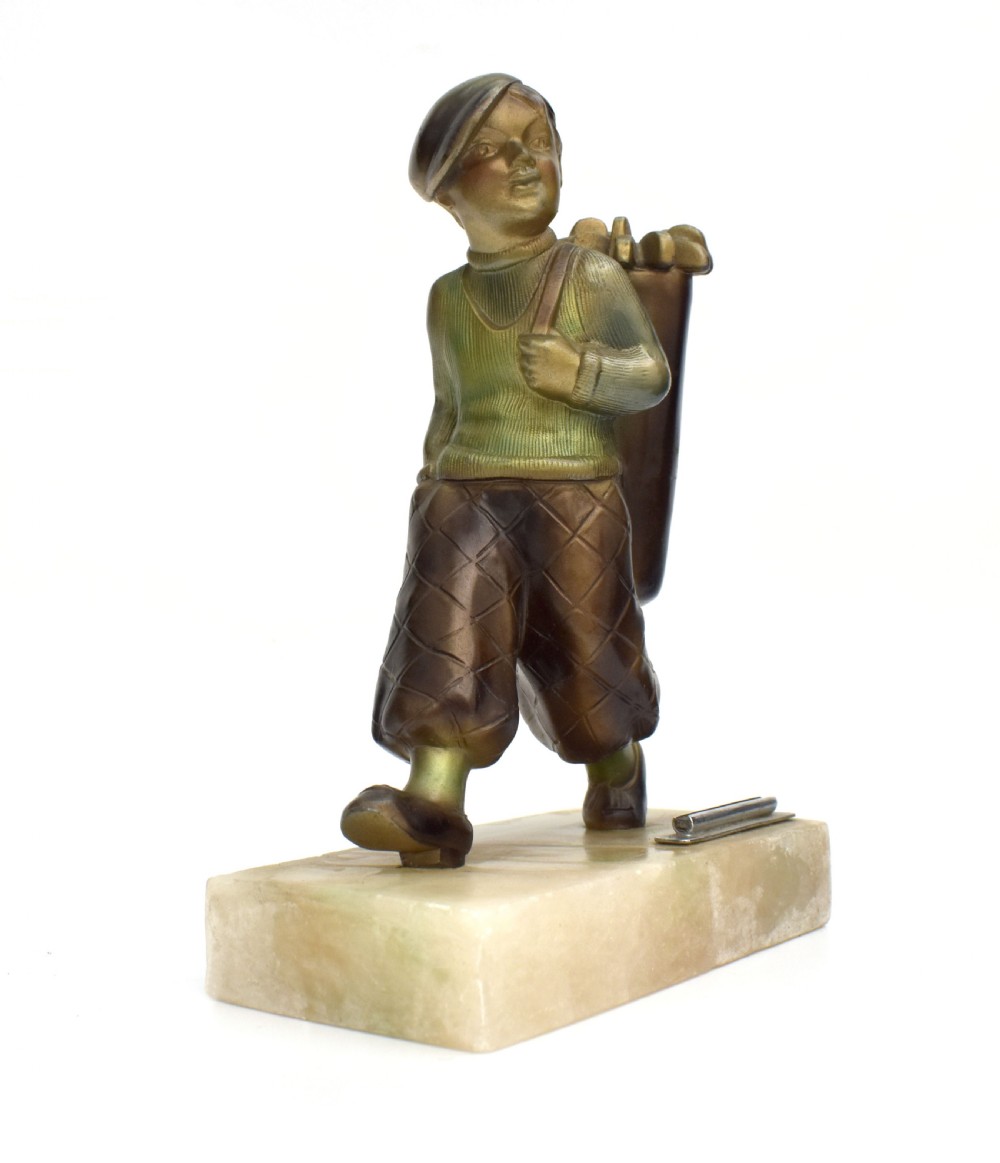 An Art Deco cold-painted bronze sculpture of a golf caddy carrying a bag, mounted on a rectangular cream onyx base with an attached metal lighter striker. View II