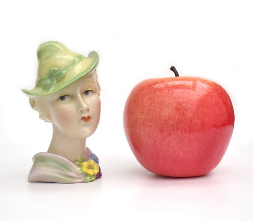 An Art Deco ceramic bust of a lady wearing a pale green hat and a floral corsage on a plain white background. View II