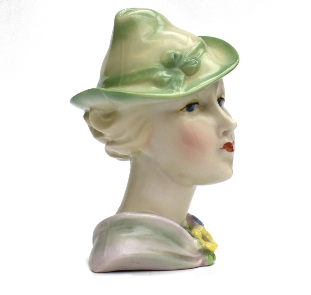 An Art Deco ceramic bust of a lady wearing a pale green hat and a floral corsage on a plain white background. View III