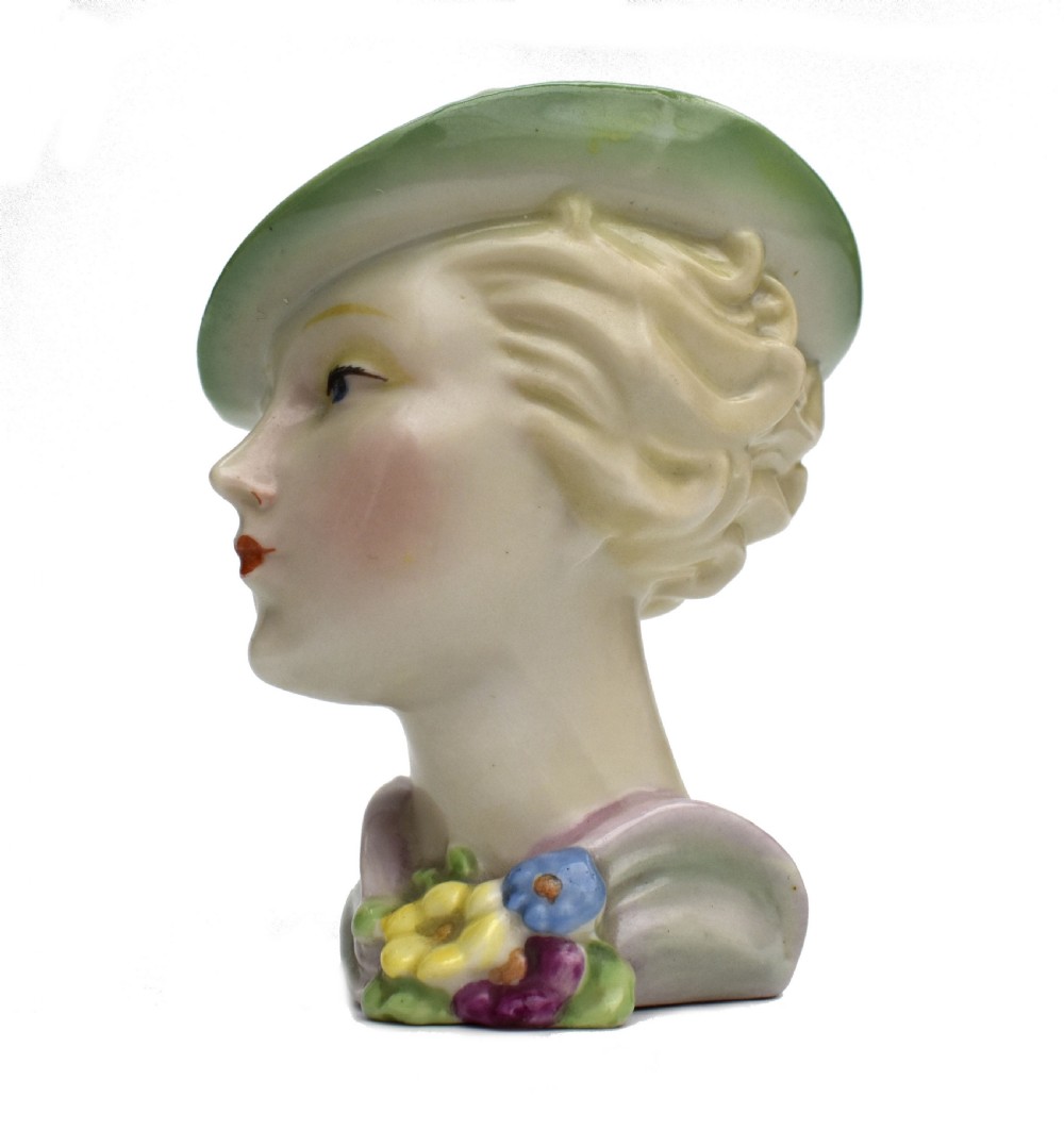 An Art Deco ceramic bust of a lady wearing a pale green hat and a floral corsage on a plain white background. View V