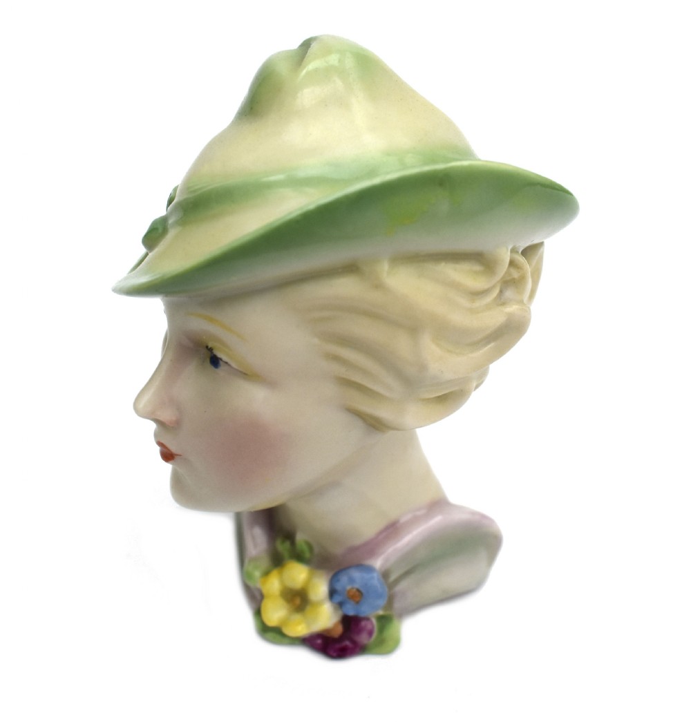 An Art Deco ceramic bust of a lady wearing a pale green hat and a floral corsage on a plain white background. View VI
