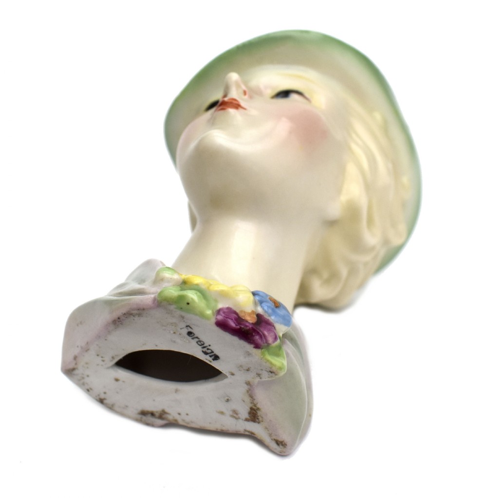 An Art Deco ceramic bust of a lady wearing a pale green hat and a floral corsage on a plain white background. View VII