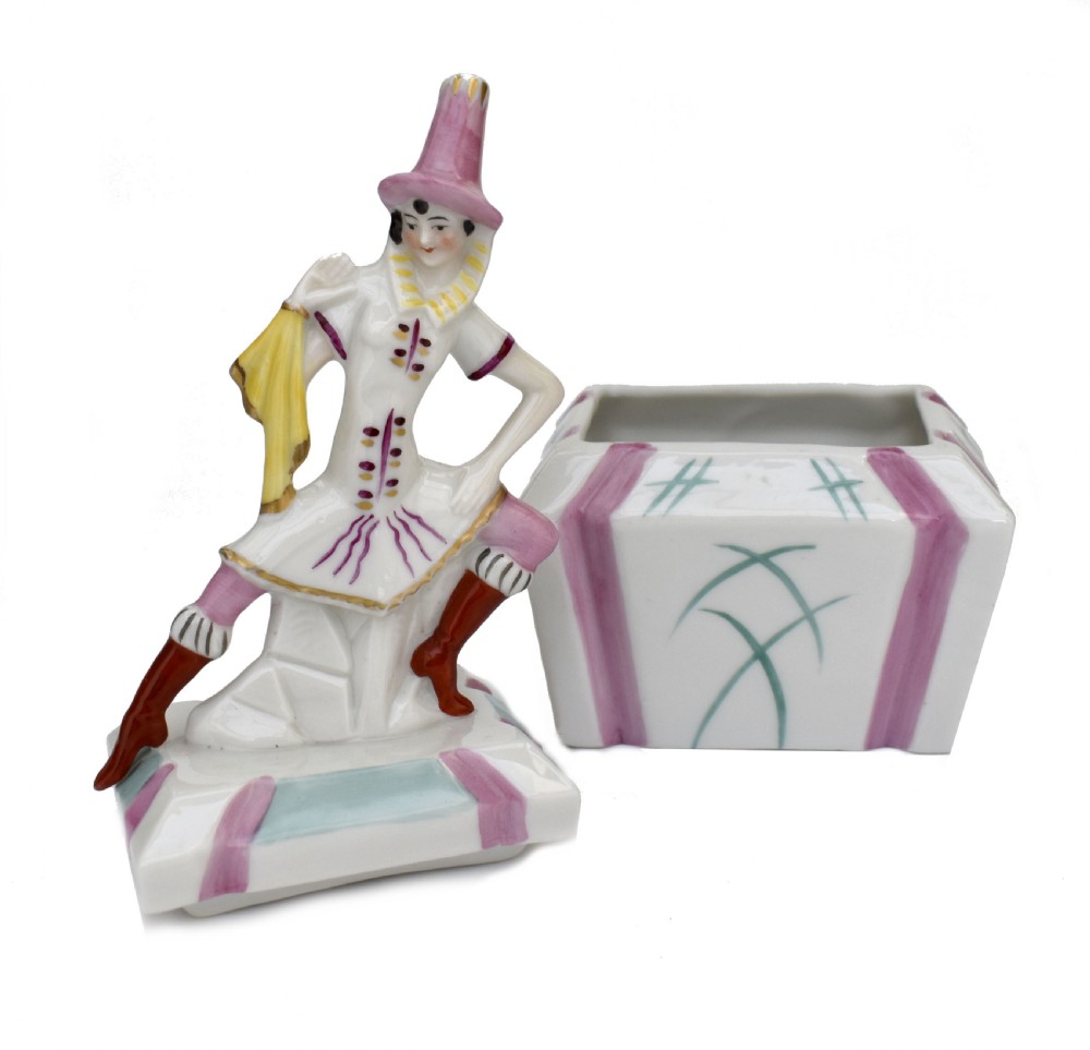 An Art Deco German porcelain trinket box featuring a hand-painted jester figure sitting atop a geometric patterned lidded base. View VI