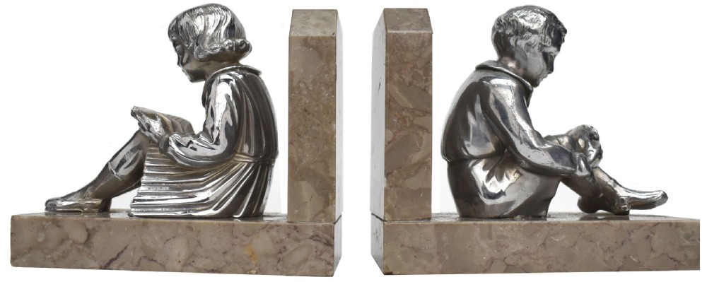 A pair of French Art Deco chromed metal bookends featuring seated children reading, mounted on beige marble bases.