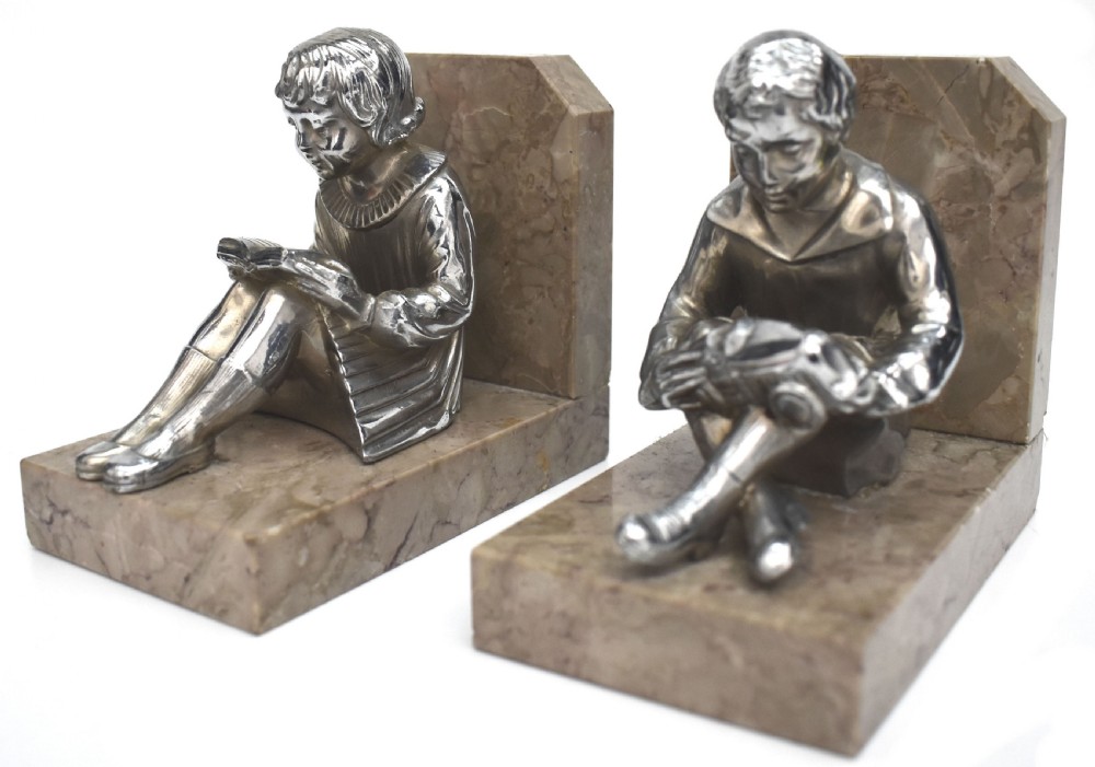 A pair of French Art Deco chromed metal bookends featuring seated children reading, mounted on beige marble bases. View II