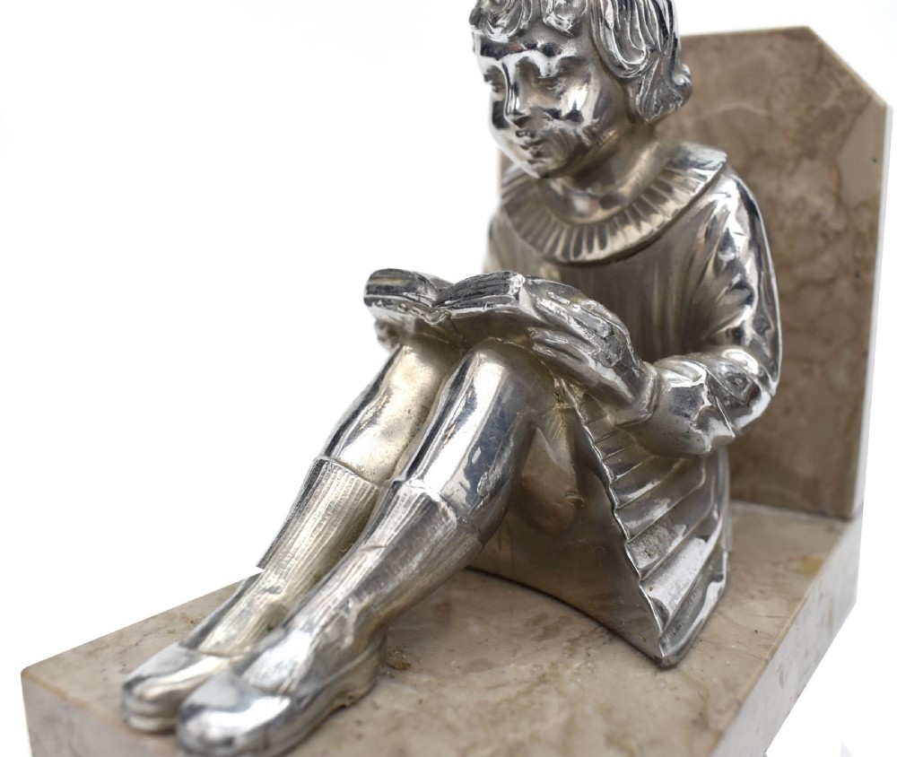 A pair of French Art Deco chromed metal bookends featuring seated children reading, mounted on beige marble bases. View III