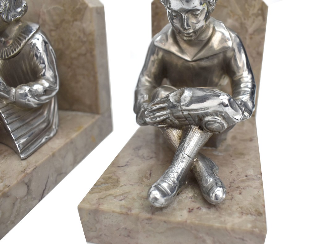 A pair of French Art Deco chromed metal bookends featuring seated children reading, mounted on beige marble bases. View IV