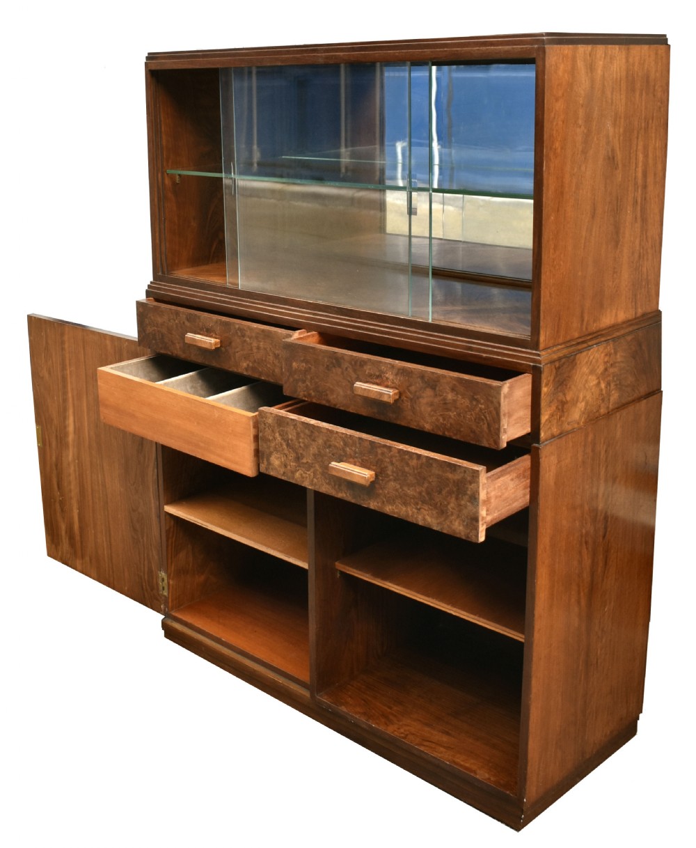 An Art Deco figured walnut drinks cabinet featuring a glass-fronted upper display section with glass shelves, drawers, and lower storage compartments. View II