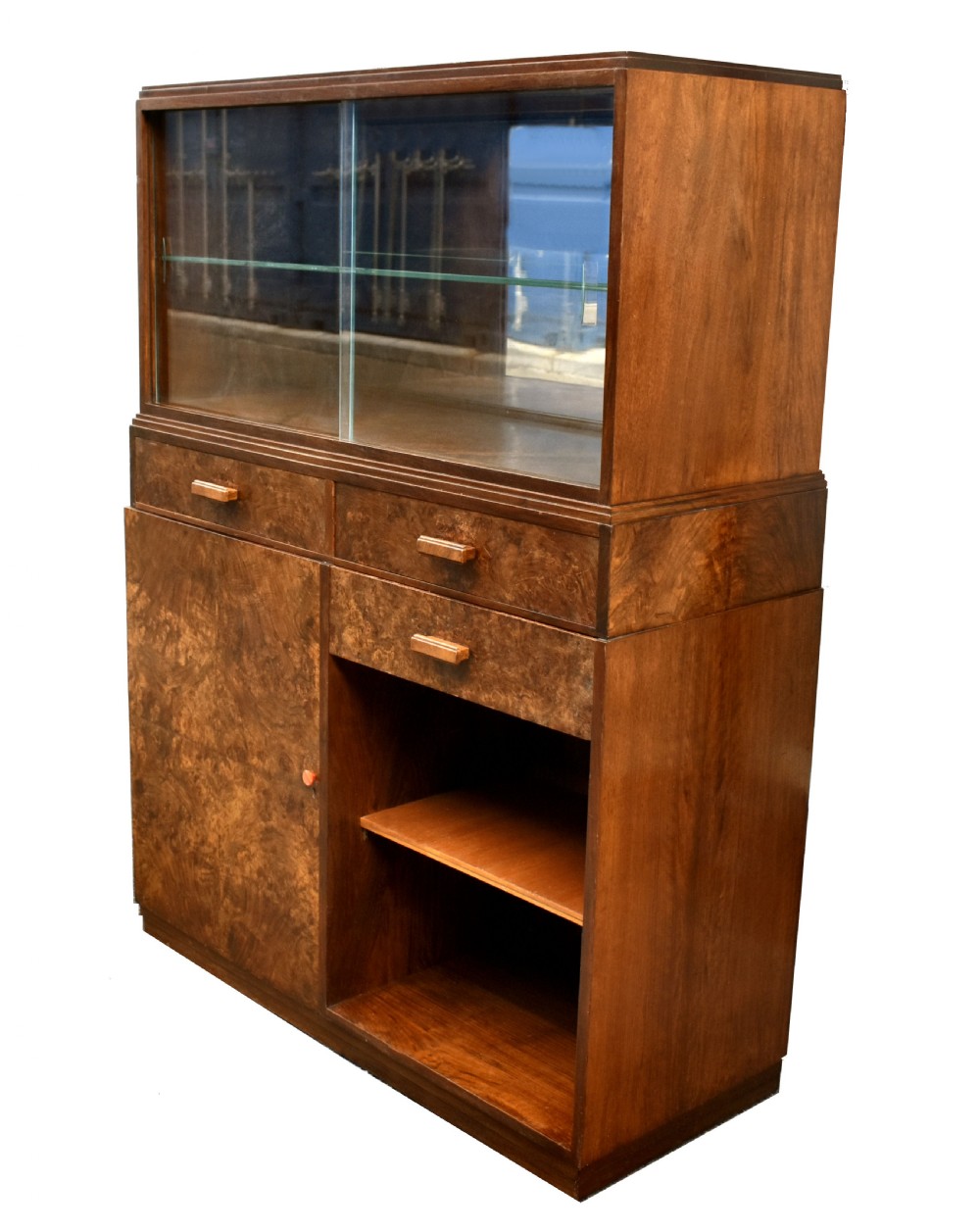 An Art Deco figured walnut drinks cabinet featuring a glass-fronted upper display section with glass shelves, drawers, and lower storage compartments. View V