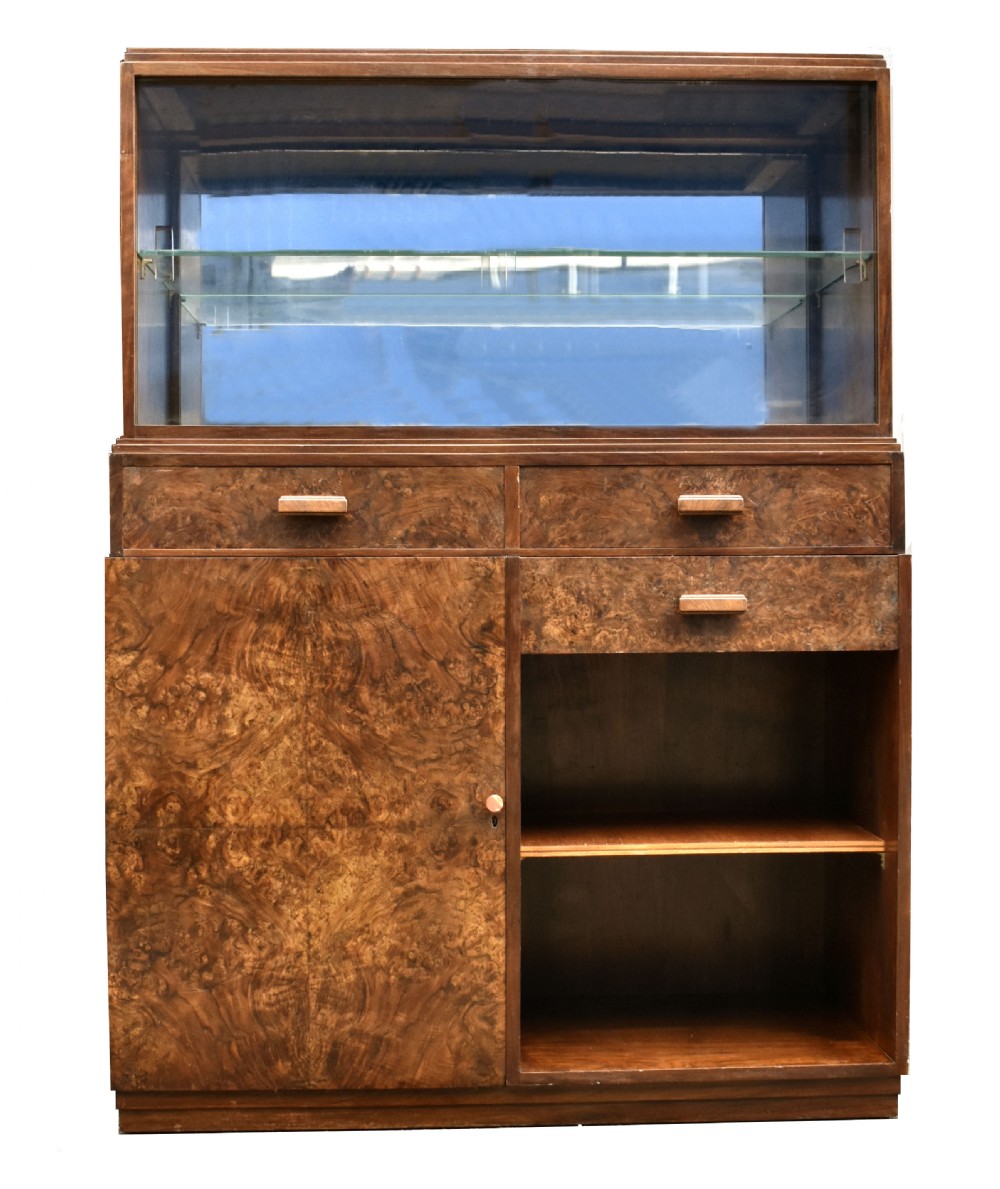 An Art Deco figured walnut drinks cabinet featuring a glass-fronted upper display section with glass shelves, drawers, and lower storage compartments. View VI