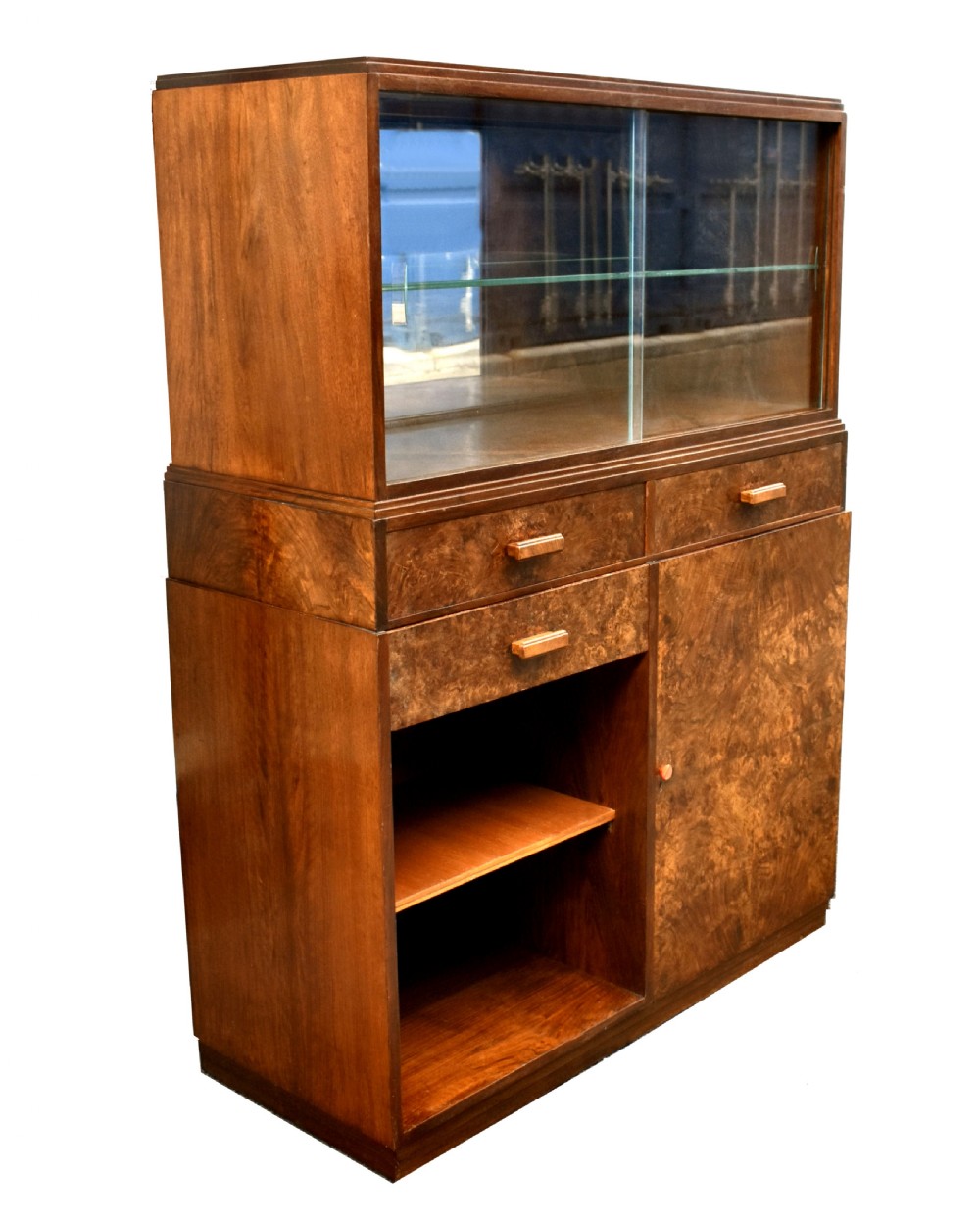 An Art Deco figured walnut drinks cabinet featuring a glass-fronted upper display section with glass shelves, drawers, and lower storage compartments. View VII