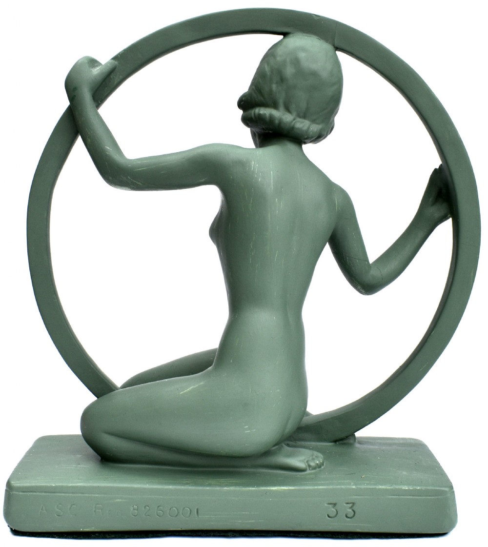 A sage green Art Deco painted plaster figurine depicting a kneeling female figure inside a circular hoop set on a rectangular base. View IV