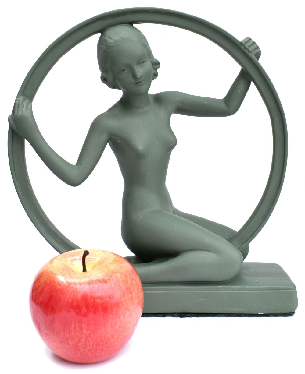 A sage green Art Deco painted plaster figurine depicting a kneeling female figure inside a circular hoop set on a rectangular base. View IX