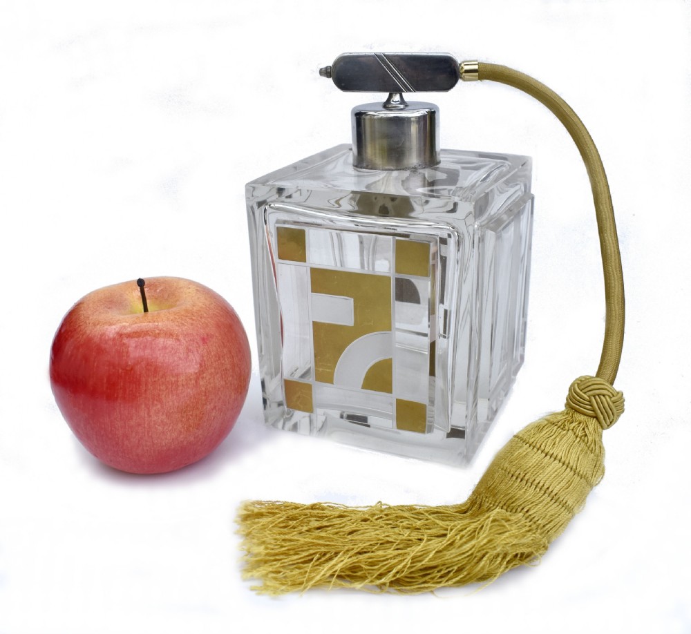 A square clear glass perfume atomizer featuring geometric gold decoration, a chrome pump mechanism, and a gold woven spray tube with a tassel. View II