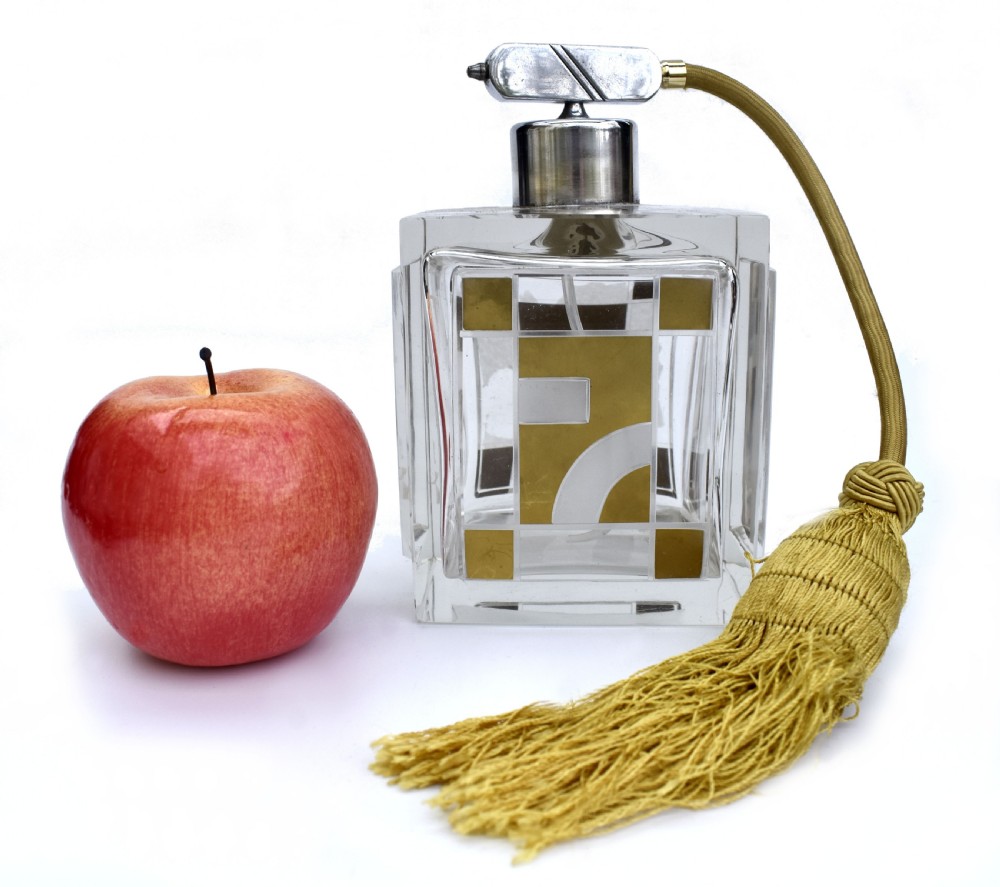 A square clear glass perfume atomizer featuring geometric gold decoration, a chrome pump mechanism, and a gold woven spray tube with a tassel. View III