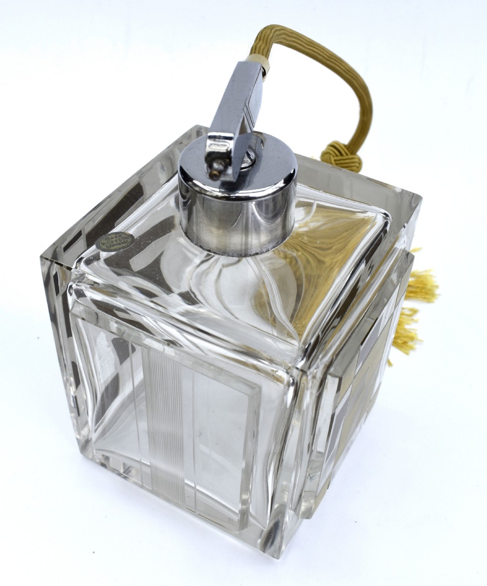 A square clear glass perfume atomizer featuring geometric gold decoration, a chrome pump mechanism, and a gold woven spray tube with a tassel. View VI
