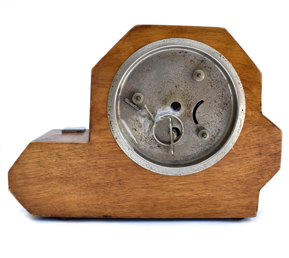 An asymmetrical Art Deco wooden mantel clock featuring two-tone wood veneers, a circular white dial with chrome bezel, and chrome foot accents. View III