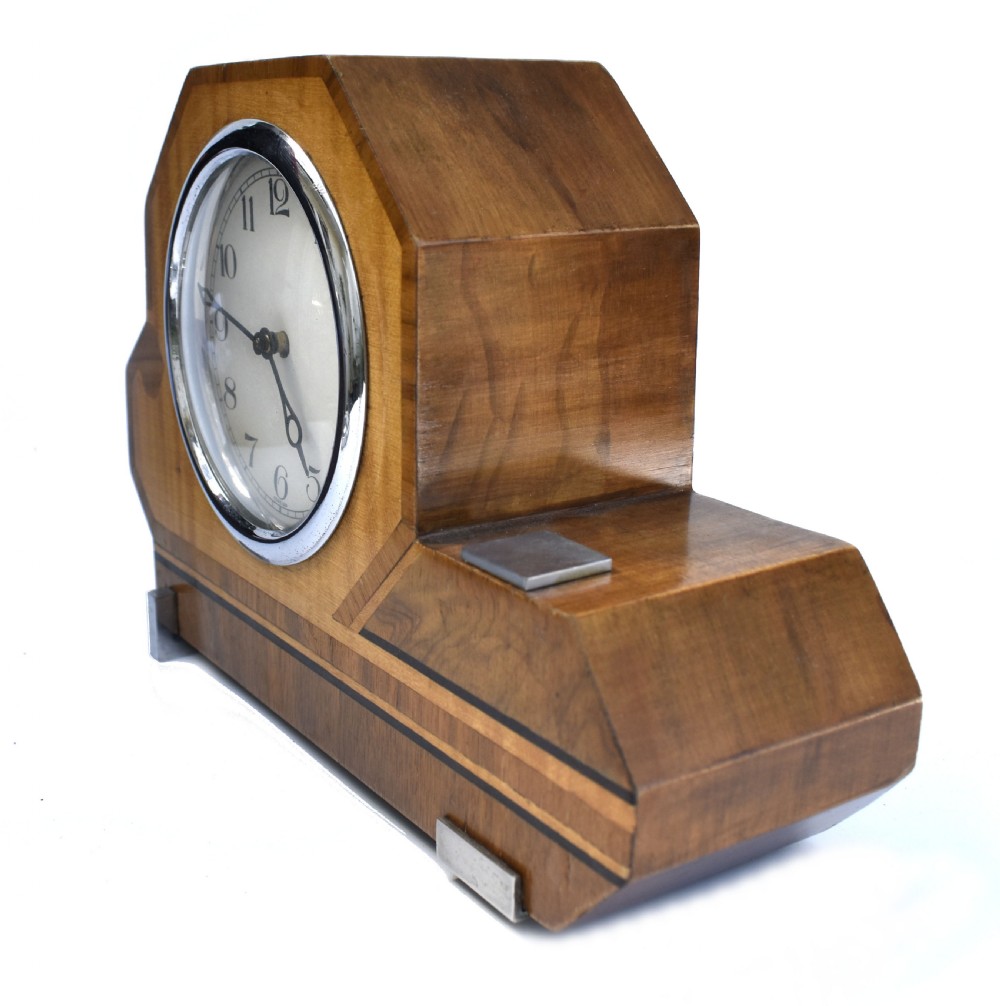 An asymmetrical Art Deco wooden mantel clock featuring two-tone wood veneers, a circular white dial with chrome bezel, and chrome foot accents. View IV