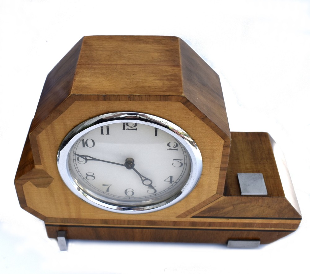 An asymmetrical Art Deco wooden mantel clock featuring two-tone wood veneers, a circular white dial with chrome bezel, and chrome foot accents. View V