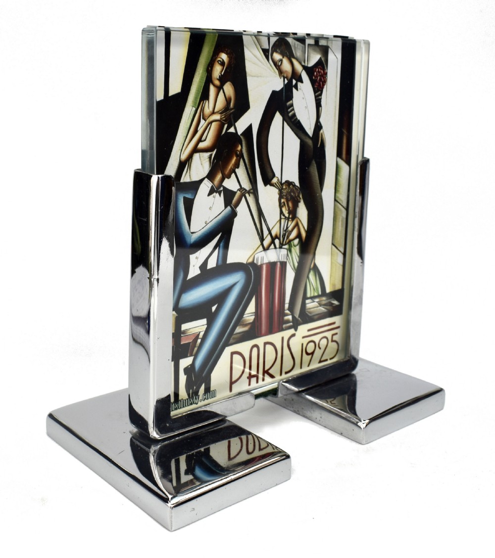 An Art Deco chrome and glass free-standing picture frame featuring a stepped metal base holding a black and white portrait photo. View II