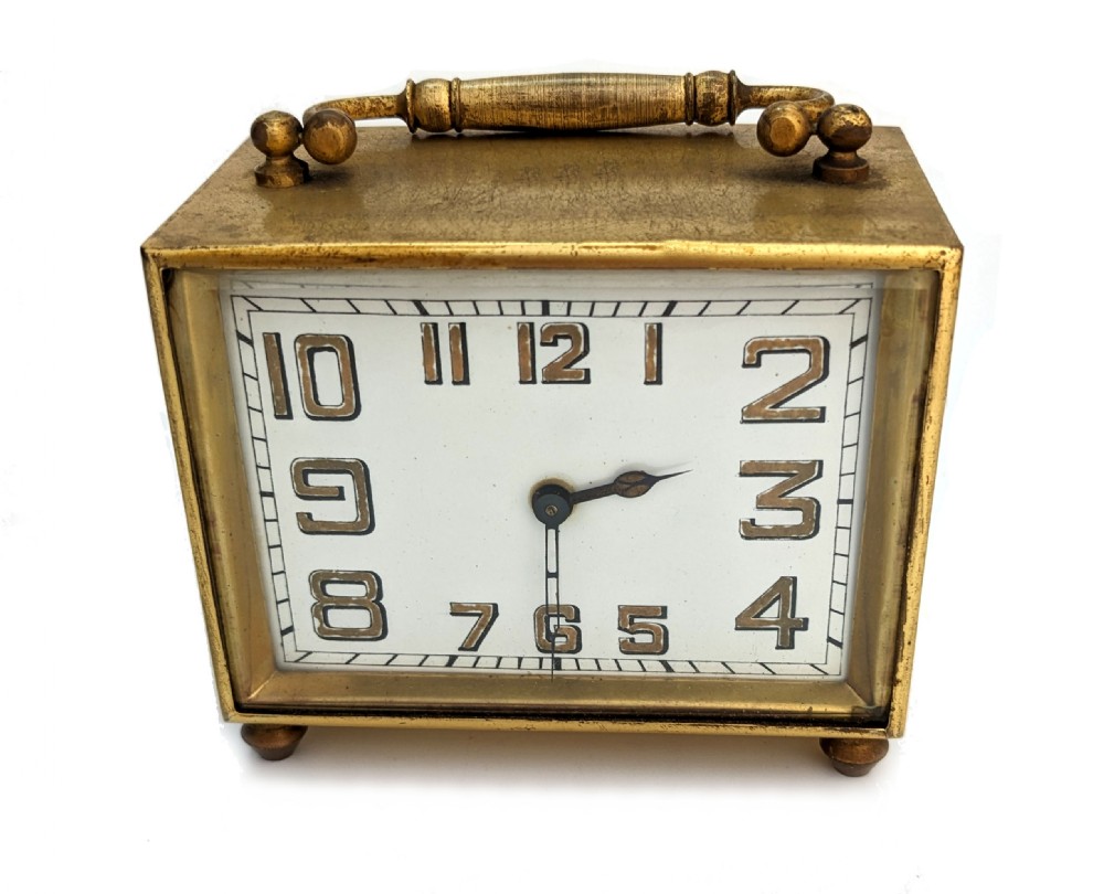 An Art Deco brass carriage clock featuring a rectangular case, top carrying handle, white face with stylized block numerals, and small bun feet. View II