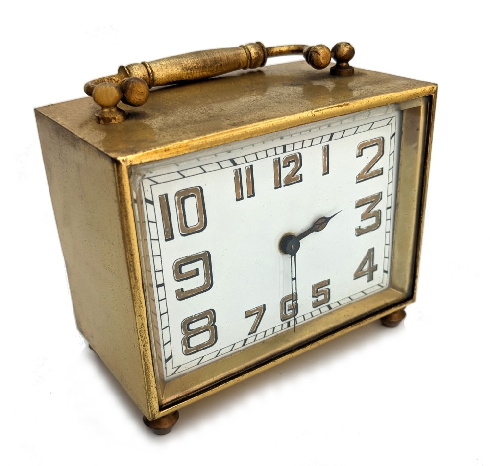 An Art Deco brass carriage clock featuring a rectangular case, top carrying handle, white face with stylized block numerals, and small bun feet. View III
