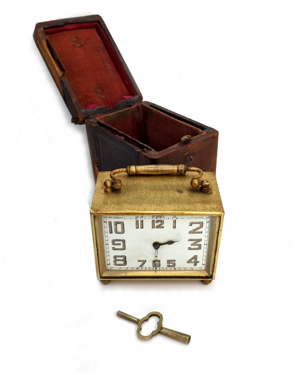 An Art Deco brass carriage clock featuring a rectangular case, top carrying handle, white face with stylized block numerals, and small bun feet. View IV