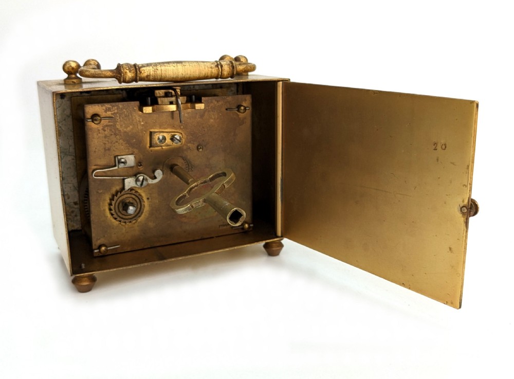 An Art Deco brass carriage clock featuring a rectangular case, top carrying handle, white face with stylized block numerals, and small bun feet. View V