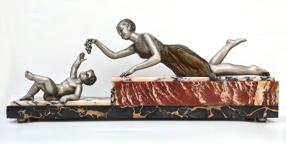 An Art Deco French spelter figural group depicting a reclining mother reaching towards her child on a stepped marble base.