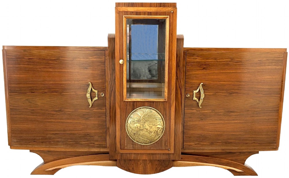 A French Art Deco walnut sideboard featuring a raised central glass vitrine above an embossed brass medallion, flanked by two veneered cupboard doors on an arched base.