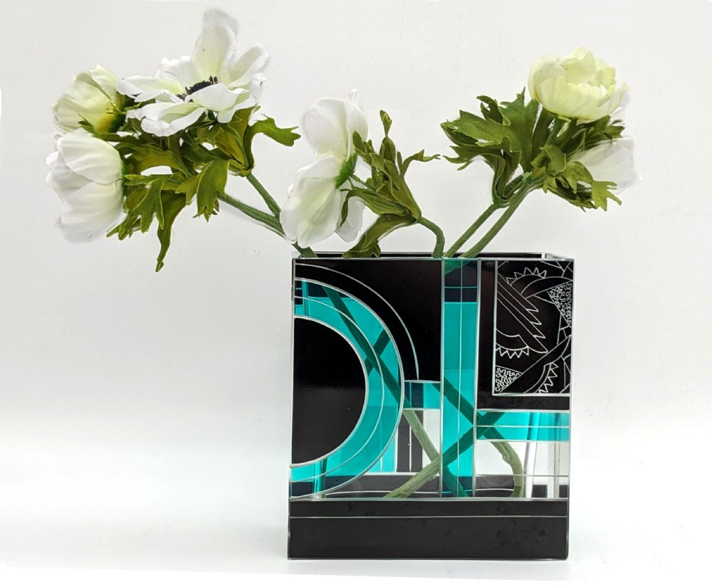 A square Art Deco glass vase decorated with geometric black and turquoise enamel shapes alongside etched patterned panels.
