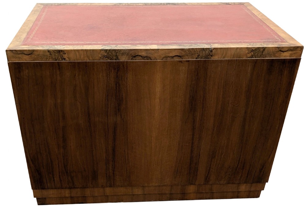 An Art Deco figured walnut writing desk featuring a red leather inset top, open curved shelves on the left pedestal, and three vertical drawers on the right. View X