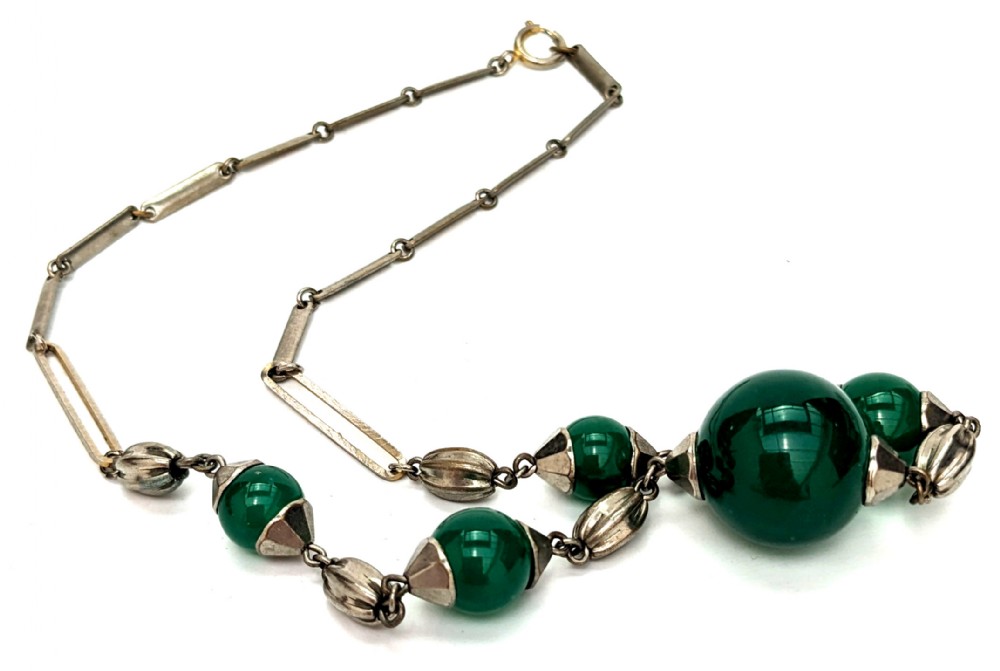 An Art Deco necklace featuring deep green glass spherical beads fitted with fluted metal caps and connected by elongated metal bar links.